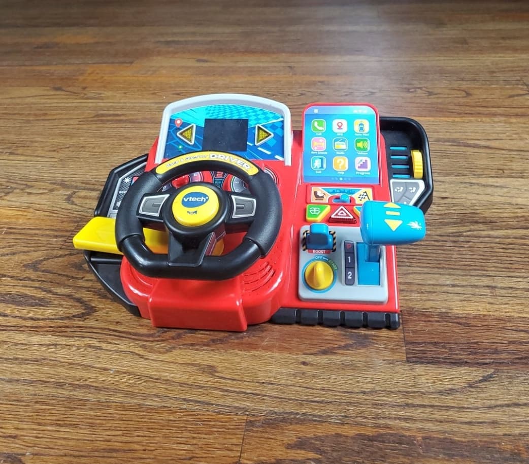 Raw phone photo of a colorful toy steering wheel on a wooden floor before Portrait Drop