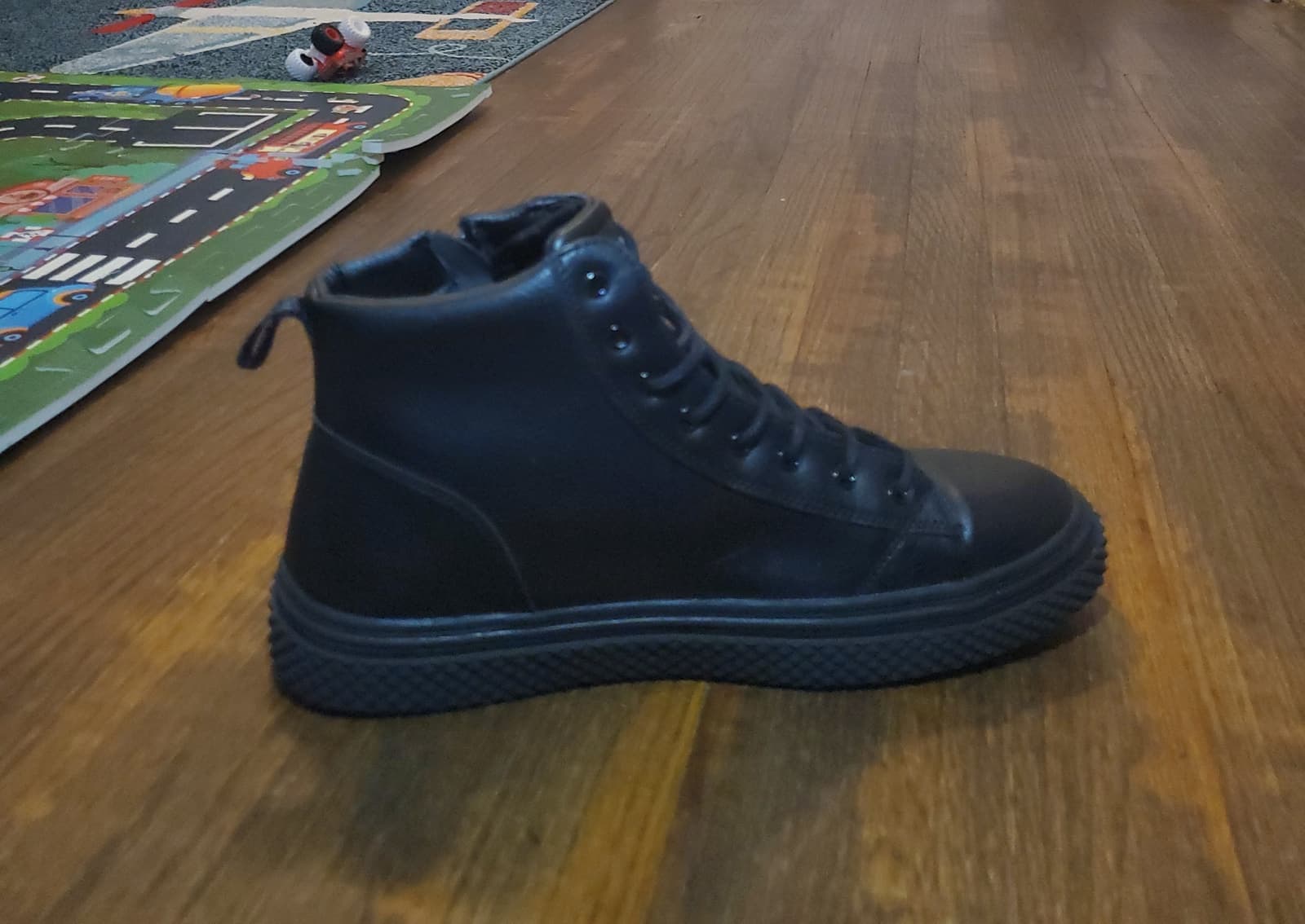 Raw phone photo of a black ankle shoe on a wooden floor before Portrait Drop