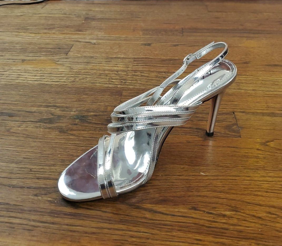 Raw Android product photo of a silver high heel on a wooden floor before Portrait Drop